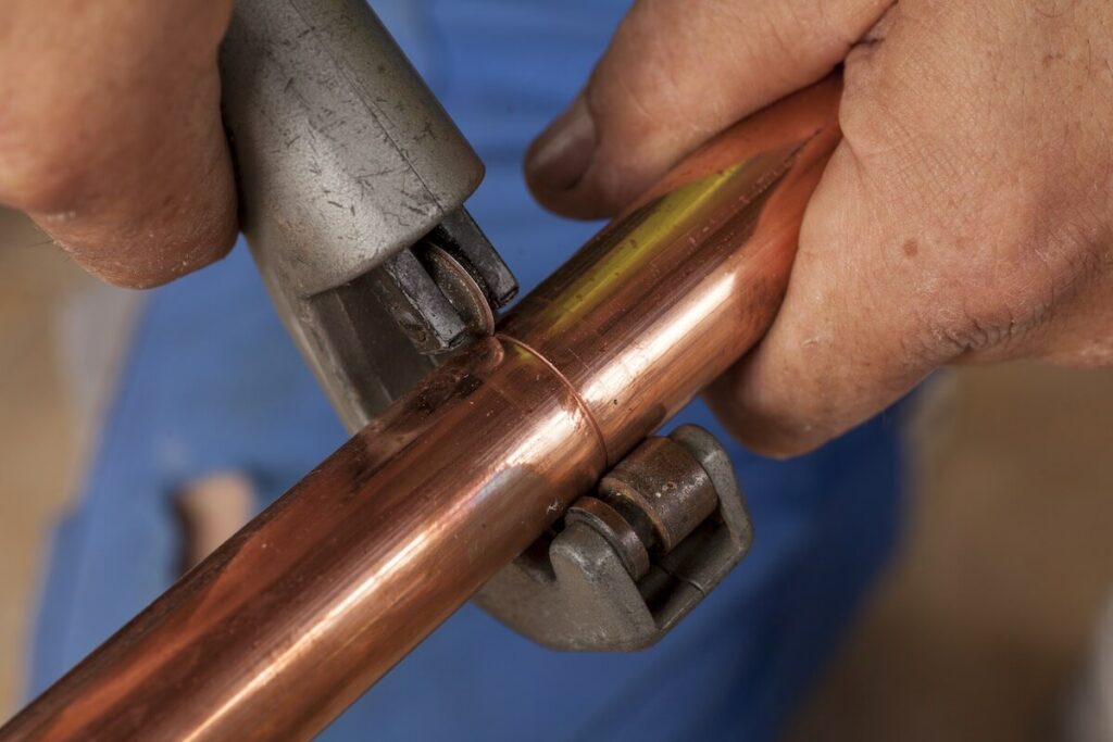 A person cutting copper pipes with a pipe cutter