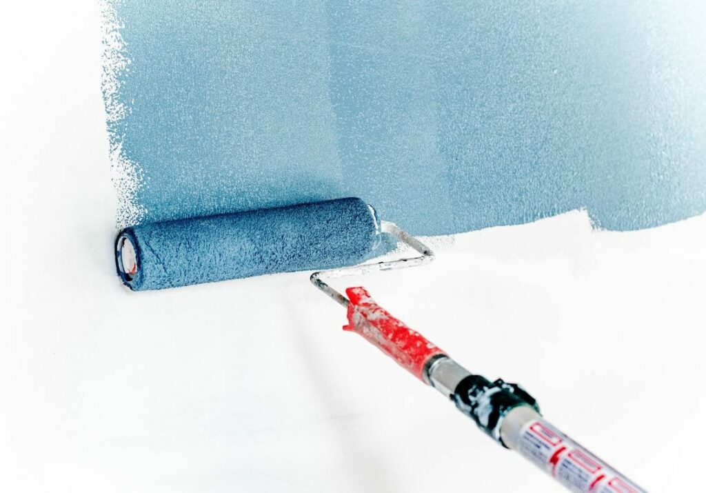 Someone off-screen using a paint roller to paint a white wall blue