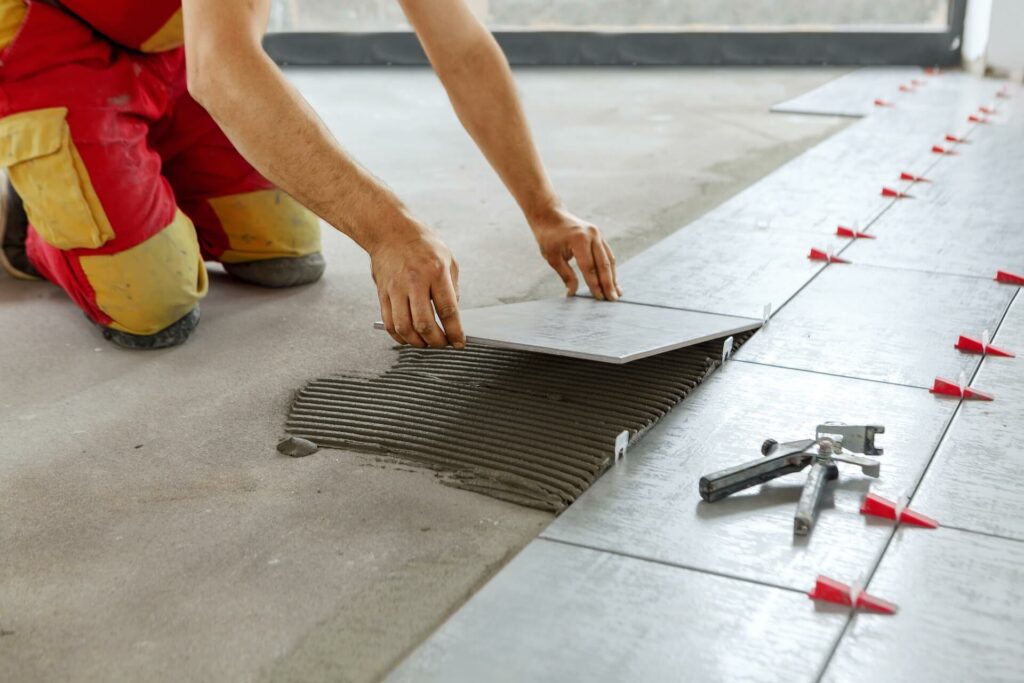 A worker installing floor tiles in a room