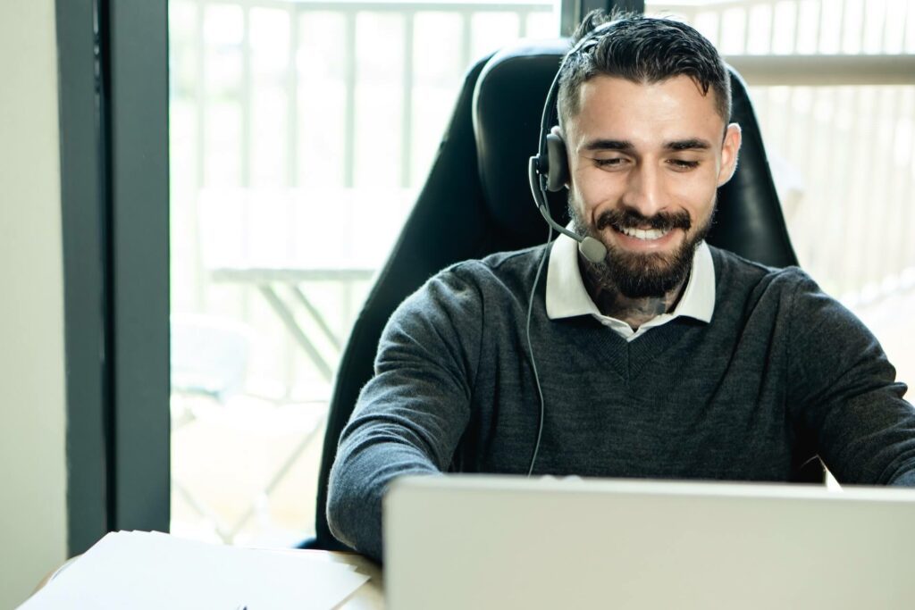 A man wearing headphones and smiling while looking at the laptop